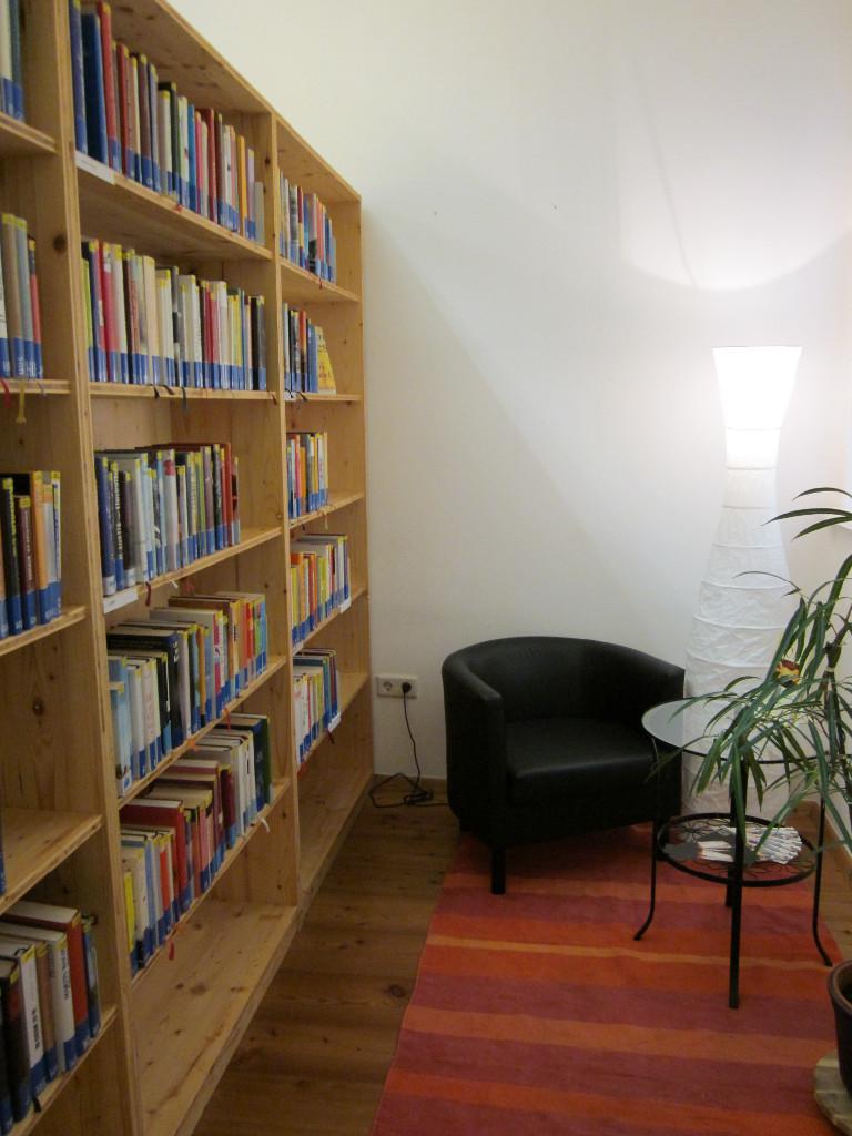 Regal auf der linken Seite des Bildes und daneben ein gemütlicher Fauteuil und ein kleiner Tisch mit Glasplatte